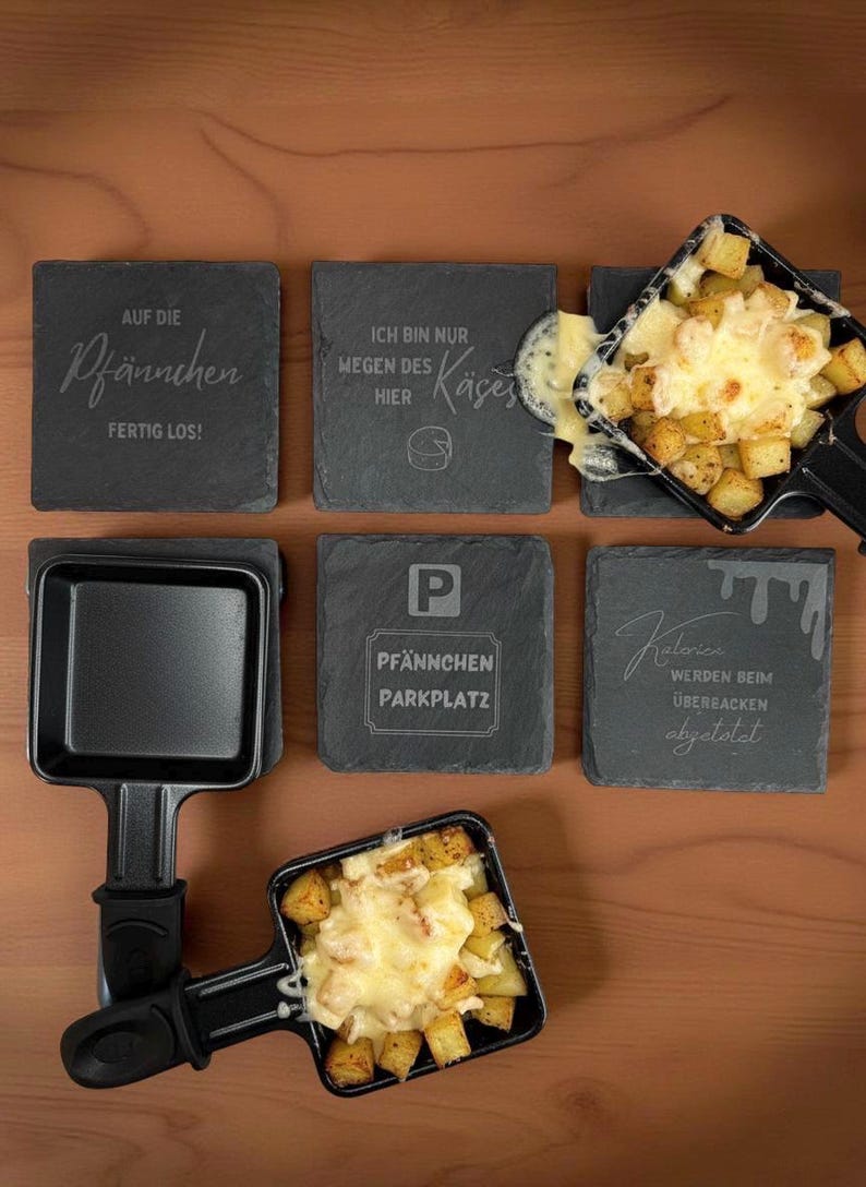 May include: A tabletop raclette grill with two filled pans of melted cheese and potatoes. The image also shows six slate coasters with engraved German text, including phrases like "Pf&auml;nnchen Parkplatz" and "Ich bin nur wegen des K&auml;ses hier."