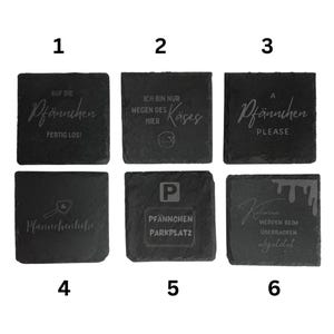 May include: A set of six square, dark gray slate coasters. Each coaster features engraved text in German. The coasters have various phrases, including "Auf die Pf&auml;nnchen fertig los!" and "Ich bin nur wegen des K&auml;ses hier."
