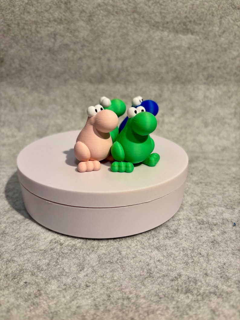 May include: A collection of colorful, cartoonish dinosaur figurines in pink, green, and blue. Each dinosaur has large white eyes and small feet. The figurines are displayed on a white, circular platform.