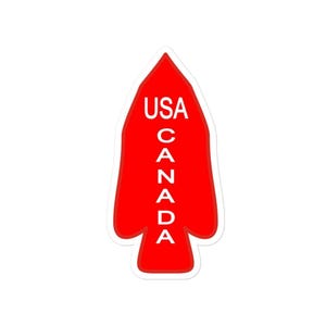 Peut inclure: Un autocollant rouge en forme de pointe de flèche. L'autocollant porte le mot "USA" en haut et le mot "CANADA" empilé verticalement en dessous en lettres blanches.