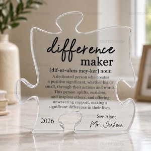 May include: Clear acrylic puzzle piece with the words "difference maker" in black script. The definition of "difference maker" is printed below. The bottom of the puzzle piece has the year "2026" and the name "Mr. Jonhson".