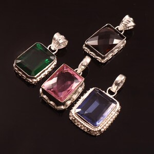Puede incluir: Cuatro colgantes de piedras preciosas con cortes rectangulares en verde, rosa, marrón y azul. Cada colgante tiene un marco decorativo plateado y un lazo para una cadena. Los colgantes se muestran sobre un fondo negro.