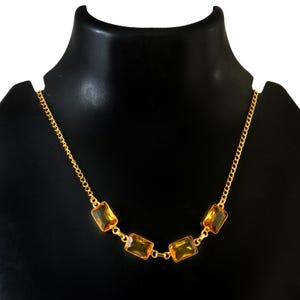 May include: A gold-toned necklace with five rectangular, amber-colored gemstones. The gemstones are set in gold and connected by a delicate gold chain. The necklace is displayed on a black mannequin.