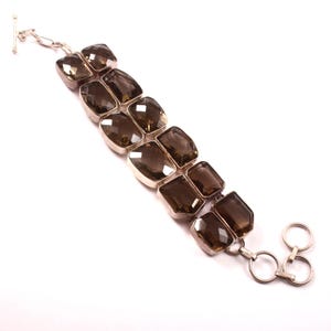 May include: A silver bracelet featuring two rows of rectangular, smoky quartz gemstones. The stones are set in silver bezels and connected by silver links. The bracelet has a toggle clasp.