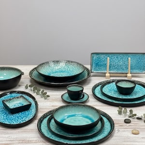 Puede incluir: Un juego completo de vajilla de cerámica turquesa y negra. El juego incluye platos, cuencos, una taza y un platillo, y una fuente rectangular. El turquesa tiene un patrón moteado y los bordes son negros.