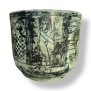 Puede incluir: Un cuenco de cerámica con un diseño verde claro y negro. El cuenco presenta figuras y patrones grabados, con una superficie texturizada. La obra de arte representa figuras humanas y formas abstractas, creando una pieza decorativa única.