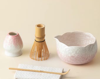 Può includere: Un set da tè matcha con una ciotola in ceramica rosa e bianca, una frusta in bambù, un piccolo contenitore in ceramica, un cucchiaio in bambù e un supporto in ceramica bianca. Per la preparazione del tè matcha giapponese.
