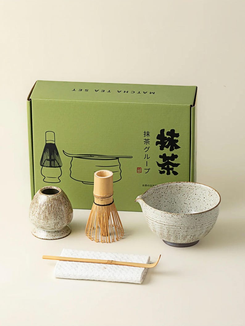 May include: A matcha tea set with a green box that reads "Matcha Tea Set" in English and Japanese. The set includes a ceramic bowl, whisk, scoop, whisk holder, and a small ceramic container. The bowl is speckled with a dark rim.