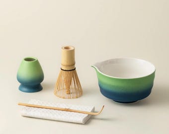 May include: A matcha tea set featuring a green and blue gradient ceramic bowl, a bamboo whisk, a whisk holder, a bamboo scoop, and a small green and blue gradient ceramic container. The set is designed for preparing matcha tea.
