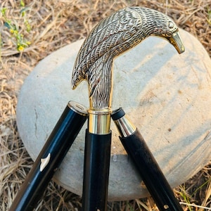 Puede incluir: Bastón decorativo con un mango de cabeza de águila de latón. El bastón tiene un eje de madera negra con detalles dorados e incrustaciones decorativas. La cabeza del águila está detallada con plumas texturizadas y un pico curvo.