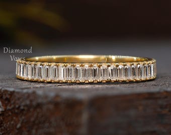 May include: A gold band ring with a continuous row of rectangular-cut, clear gemstones. The ring is set on a dark, textured surface. The words "Diamond Vows" are visible in the upper left corner.