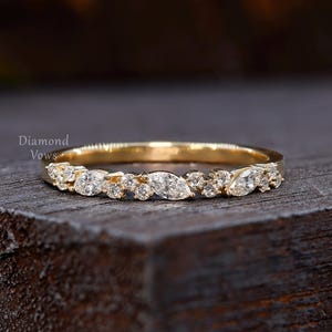 May include: A gold band ring adorned with diamonds. The ring showcases a pattern of marquise and round-cut diamonds along the top. It is presented on a dark wooden surface. The text "Diamond Vows" is visible in the upper left corner.