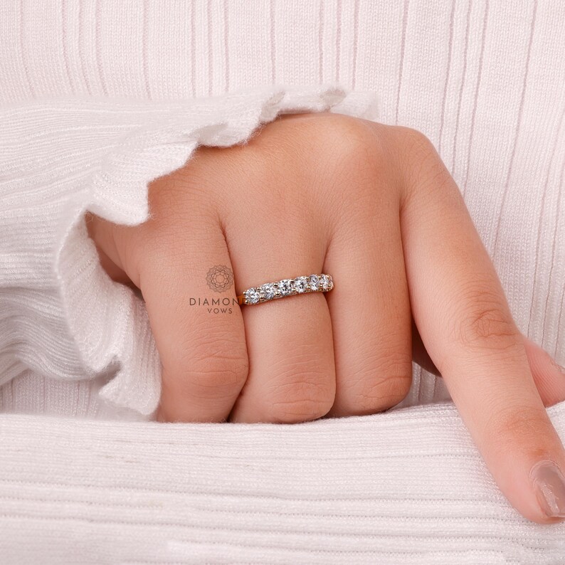 May include: A gold band ring with five clear gemstones. The ring is on a person's finger, with the hand resting on a white sweater. The ring is a piece of jewelry.