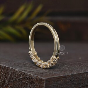 May include: A gold-colored ring with a curved design. The ring features a row of small, clear gemstones set along the bottom curve. The ring is displayed on a dark wooden surface. The text "DIAMOND VOWS" is visible.