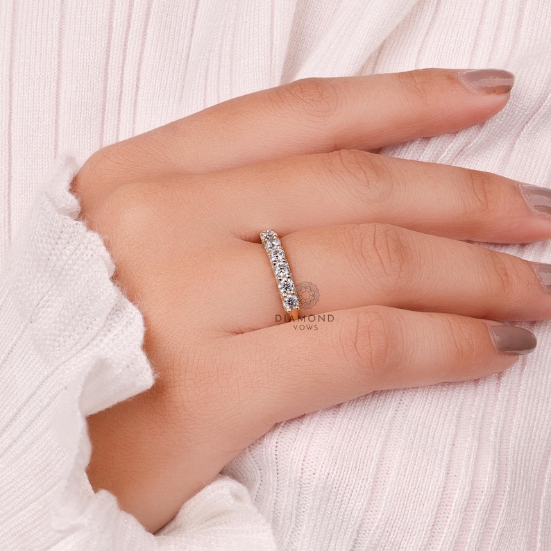 May include: A gold band ring with multiple clear gemstones. The ring is on a person's finger, with the Diamond Vows logo visible. The ring is set against a white background.