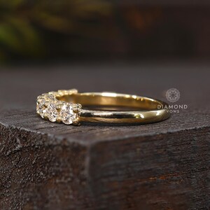 May include: A gold band ring with several small diamonds set across the top. The ring is displayed on a dark wooden surface. The words "DIAMOND VOWS" are printed on the right side of the image.