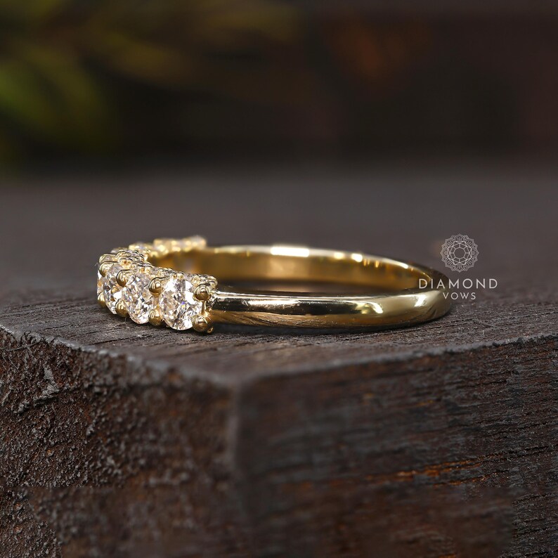 May include: A gold band ring with several small diamonds set across the top. The ring is displayed on a dark wooden surface. The words "DIAMOND VOWS" are printed on the right side of the image.