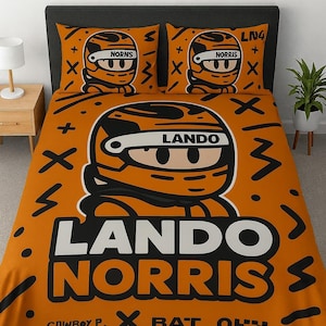 May include: Orange bedding set featuring a cartoon illustration of a race car driver's helmet with the name "LANDO NORRIS" in large white letters. The set includes a duvet cover and two pillowcases with the driver's name and helmet design.