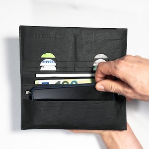 Könnte beinhalten: Schwarze Ledergeldbörse mit mehreren Kartenfächern, einer Reißverschlusstasche und einem großen Fach für ein Smartphone. Die Geldbörse ist geöffnet und zeigt Karten und Bargeld. Der Markenname "HOLZLEDER" ist oben eingeprägt.