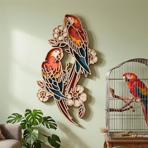 May include: Wooden wall art featuring three colorful parrots perched on flowering branches. The parrots have red, yellow, and blue plumage. A real parrot sits in a cage nearby. The wall art is a decorative accent.