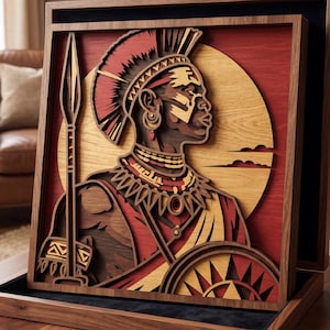 Op de afbeelding: Een gelaagd houten kunstwerk dat een profiel toont van een persoon in traditionele kledij, met een speer en schild. Het kunstwerk heeft een rood, bruin en tan kleurenpalet, met een cirkelvormig zonontwerp op de achtergrond. Het stuk wordt in een houten frame getoond.