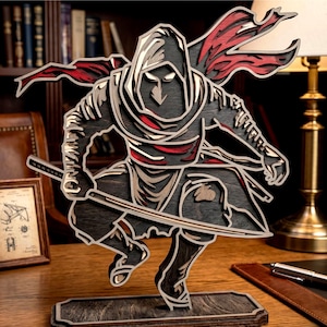 May include: A wooden ninja figurine in a crouching pose, holding two swords. The figure is layered with black, red, and tan wood, and is mounted on a rectangular base. The ninja wears a hooded cloak.