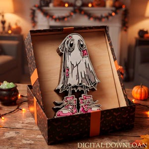 Puede incluir: Un recorte de madera en capas de un fantasma de dibujos animados con zapatillas rosas, presentado dentro de una caja de regalo negra con cintas naranjas. El fantasma tiene parches cosidos y ojos grandes, archivo de descarga digital.