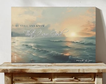 May include: A canvas print depicting a serene ocean scene at sunset. The artwork features soft blues, greens, and oranges, with the text "BE STILL AND KNOW That I am God" and "PSALM 46:10" in elegant white script. The print is displayed on a wooden table.