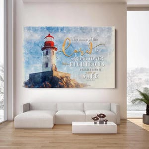 May include: A canvas print in a watercolour style, depicting a lighthouse with a red top and white tower against a blue sky. The text reads "The name of the Lord is a strong tower the righteous runneth into it and is safe."