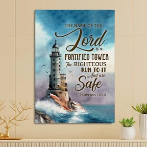 May include: A framed canvas print with a watercolour painting of a lighthouse on a rocky shore. The artwork includes the text "THE NAME OF THE Lord is a FORTIFIED TOWER The RIGHTEOUS RUN TO IT And are Safe PROVERBS 18:10."