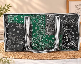May include: A rectangular quilted tote bag featuring a patchwork design of green and black bandana-style paisley patterns. The bag is finished with black and white striped fabric trim along the edges and includes two matching striped carry handles.