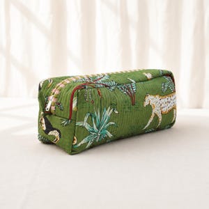May include: A rectangular quilted zipped pouch in a deep green hue, featuring a repeating pattern of spotted leopards, tropical plants, and toucans. The bag has a structured shape with a white zip pull and a red fabric trim along the edge.