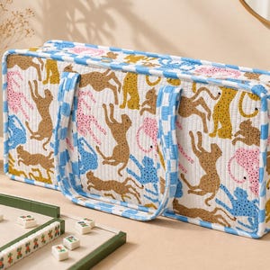 May include: A rectangular quilted fabric storage bag featuring a repeating pattern of stylized leopards in shades of brown, pink, and blue on a white background, finished with a blue and white checkered trim and matching fabric handles.