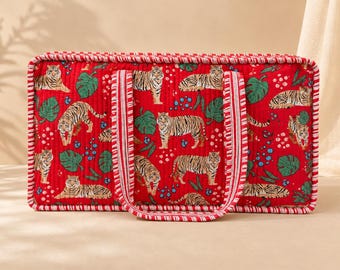May include: A rectangular quilted tote bag in a vibrant red color featuring a repeating pattern of tigers, green monstera leaves, and small blue dots. The bag has two matching red and white striped fabric handles and a matching striped trim.