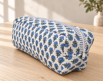 May include: A rectangular quilted zippered pouch featuring a repeating pattern of small blue flowers with green stems on a white background, accented by a blue and white striped fabric trim along the zipper closure and side panel.
