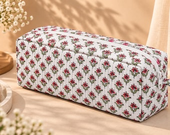 May include: A rectangular quilted fabric pouch featuring a repeating floral pattern of small red flowers with green stems and leaves on a white background. The pouch has a white zipper closure along the top edge and vertical quilted stitching lines.