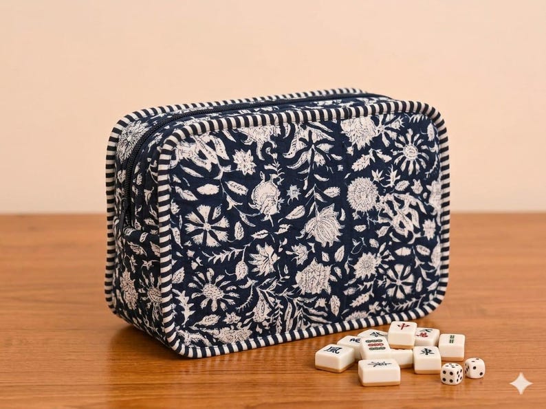 May include: A rectangular navy blue fabric pouch featuring a white floral pattern and striped piping along the edges. The pouch has a zippered closure and is accompanied by a small collection of white mahjong tiles and two dice.