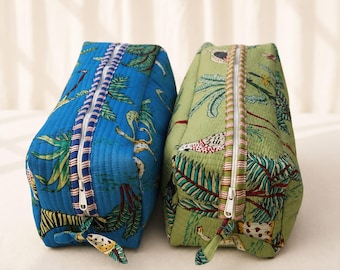 May include: Two rectangular quilted toiletry bags featuring a tropical print with palm trees and animals. One bag is bright blue with a striped zipper trim, and the other is sage green with a matching striped zipper trim and white zipper pulls.