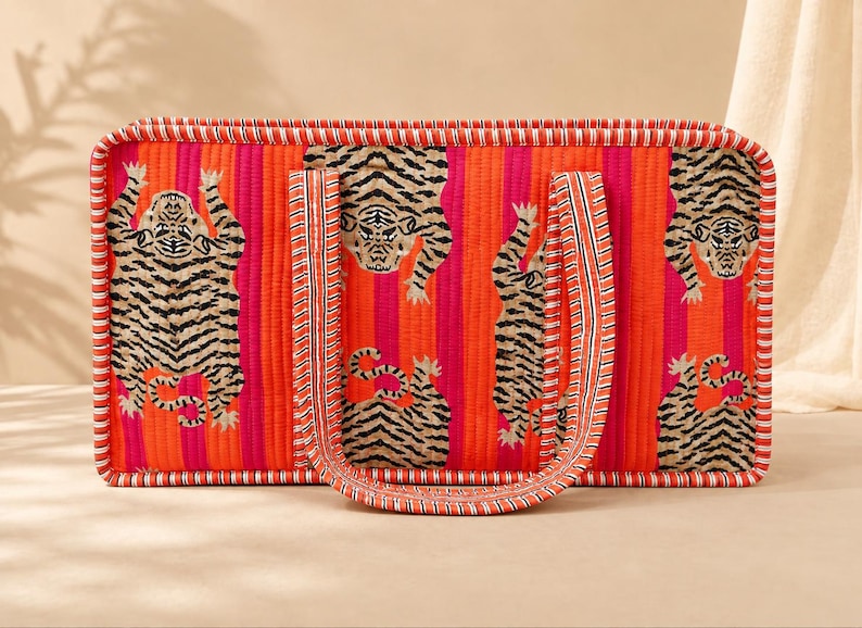 May include: A rectangular quilted tote bag featuring vertical stripes in bright orange and hot pink. The bag is decorated with a repeating pattern of black and beige tiger illustrations and has two matching fabric handles with striped trim.
