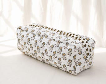 May include: A rectangular quilted fabric pouch featuring a white base with a repeating floral pattern in shades of yellow, blue, and green. The pouch has a zippered closure along the top edge with a dark brown and white checkered trim detail.