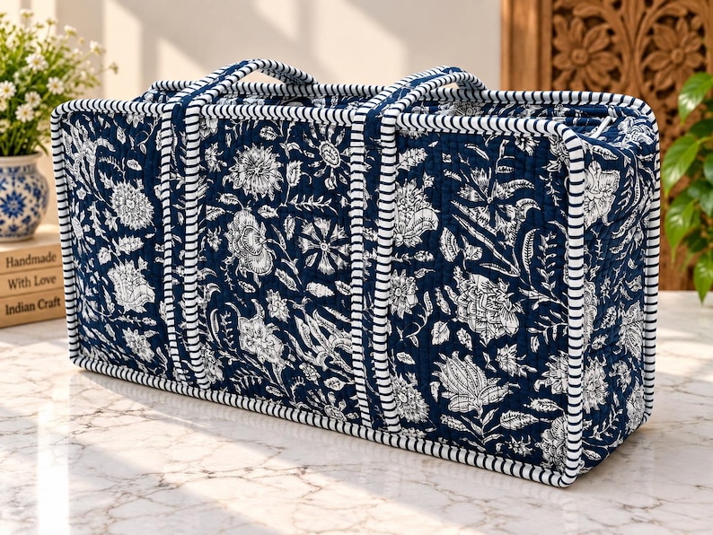 May include: A rectangular quilted storage bag featuring a dark navy blue fabric with a white floral print. The bag has two top handles and is finished with white and navy blue striped piping along all edges and seams for structure.