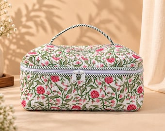 May include: A rectangular quilted travel case featuring a white base with a repeating floral pattern of pink flowers and green leafy vines. The bag includes a top handle, a white zipper closure with two white pulls, and matching green and white piping.