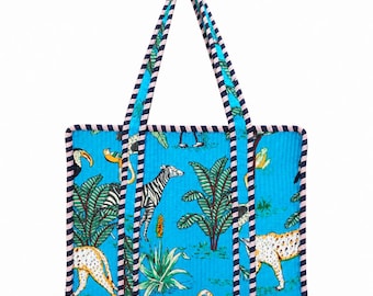 May include: A quilted tote bag in bright blue featuring a jungle-themed print with zebras, leopards, toucans, and tropical plants. The bag has two long handles and edges trimmed with a navy blue and white striped fabric pattern.