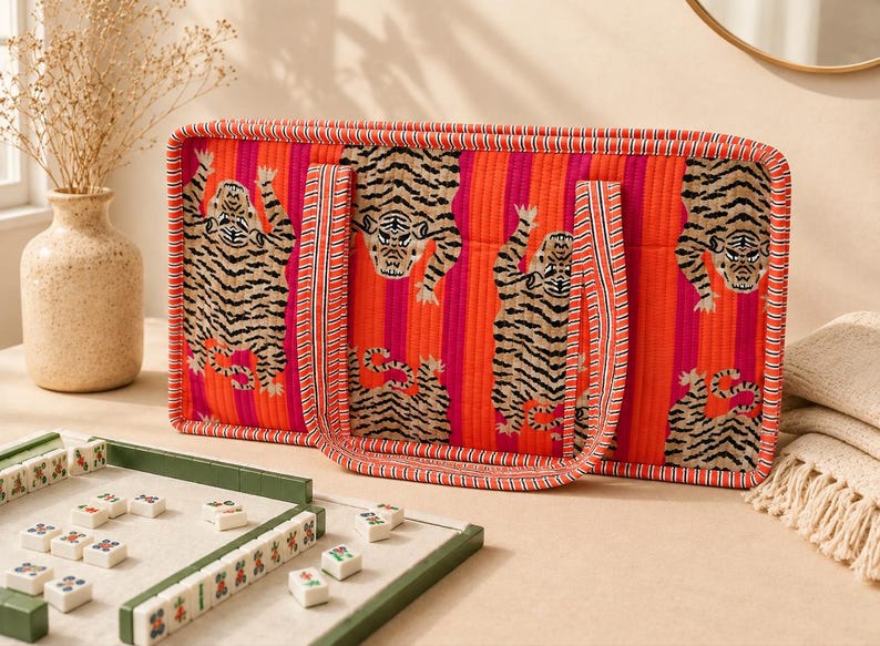 May include: A rectangular quilted tote bag featuring a vibrant orange and pink vertical striped pattern with a repeating tiger motif. The bag has two matching fabric handles and is finished with a striped fabric trim along the edges.