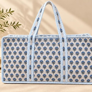 May include: A rectangular tote bag featuring a repeating blue floral pattern on a light beige background. The bag has two handles and edges trimmed with a light blue and white gingham check fabric, providing a structured appearance.