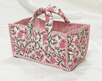 May include: A rectangular quilted fabric basket featuring a floral pattern with pink flowers and green vines on a white background. The basket has two matching fabric handles and is trimmed with a pink and white striped fabric along the edges.