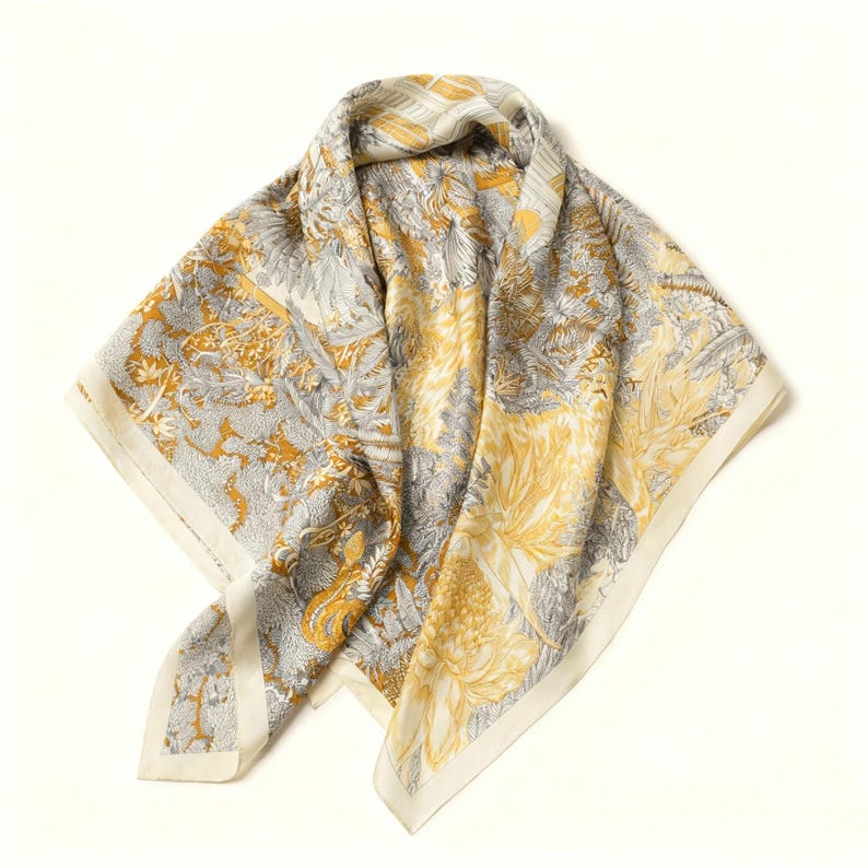 Puede incluir: Pa&ntilde;uelo cuadrado de seda con un dise&ntilde;o floral y de hojas en tonos amarillo, gris y crema. El pa&ntilde;uelo presenta un patr&oacute;n detallado con un borde crema. Est&aacute; doblado y drapeado, mostrando el intrincado dise&ntilde;o.