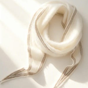 Pode incluir: Um cachecol branco sujo com listras castanhas sutis. O cachecol é drapeado em forma circular, com as pontas penduradas. O tecido parece leve e arejado, perfeito para adicionar um toque de elegância a qualquer roupa.