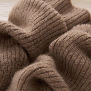 May include: Close-up of a soft, ribbed knit fabric in a warm, earthy brown color. The texture of the knitwear is visible, with prominent vertical ribbing. The fabric appears to be thick and cozy, suggesting a sweater or scarf.