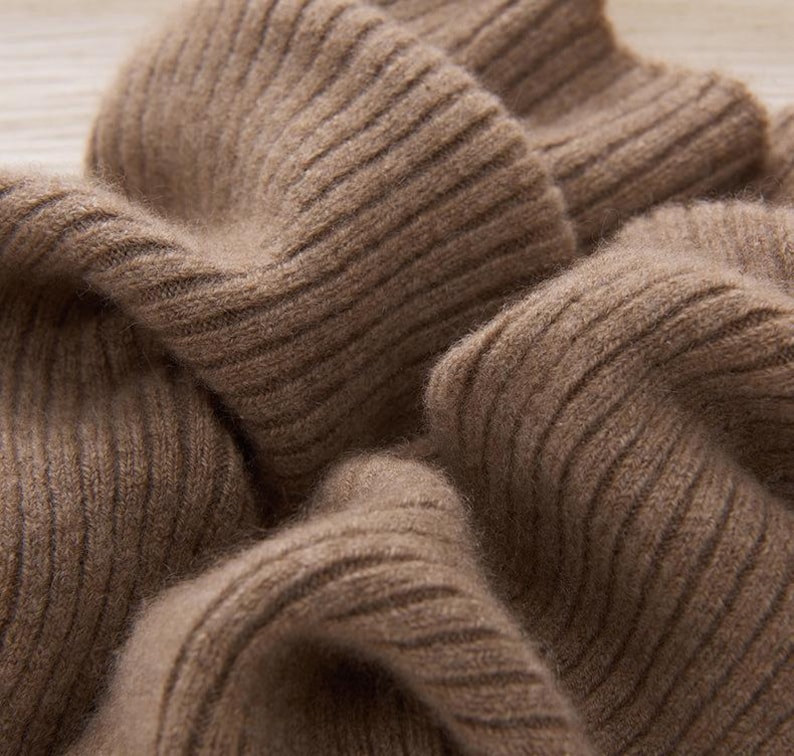 May include: Close-up of a soft, ribbed knit fabric in a warm, earthy brown color. The texture of the knitwear is visible, with prominent vertical ribbing. The fabric appears to be thick and cozy, suggesting a sweater or scarf.